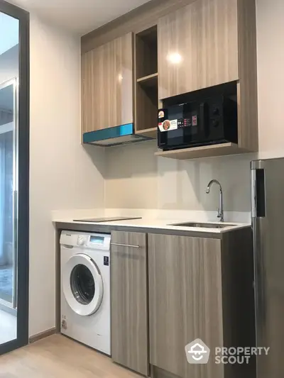 Modern kitchen with washing machine and built-in microwave in sleek cabinetry