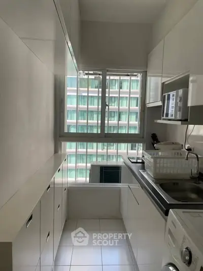 Modern kitchen with sleek white cabinets and large window offering natural light.