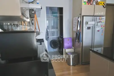 Modern kitchen with sleek appliances and adjacent laundry area, featuring a washing machine and ample storage.
