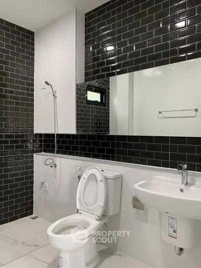 Modern bathroom with sleek black and white tiles, featuring a toilet and sink.