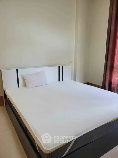 Spacious bedroom with a comfortable bed and natural light from a window with curtains.