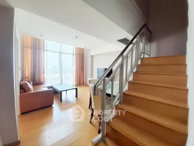 Spacious living room with modern staircase and large windows offering city views.