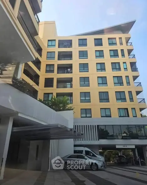 Modern apartment building with balconies and parking area in urban setting.