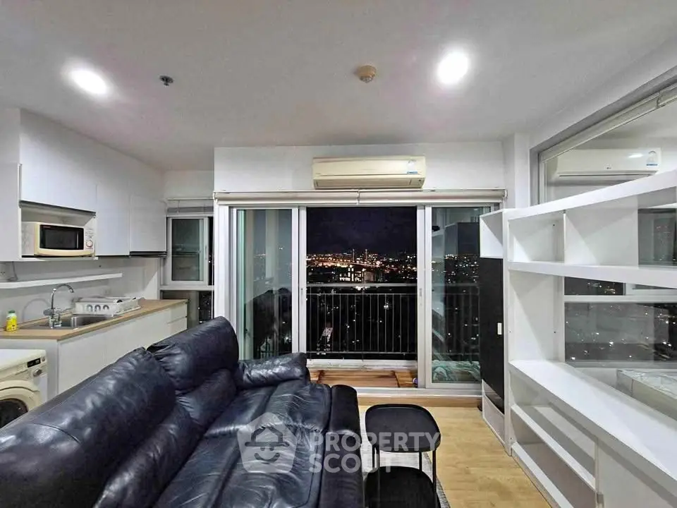 Modern living room with city view, featuring sleek black leather sofa and open kitchen layout.