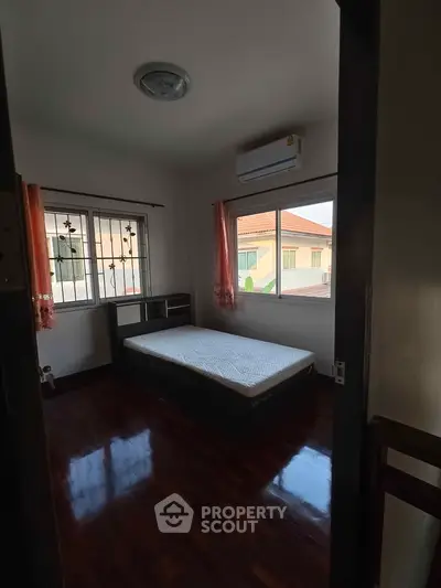Cozy bedroom with wooden flooring and large windows offering natural light.