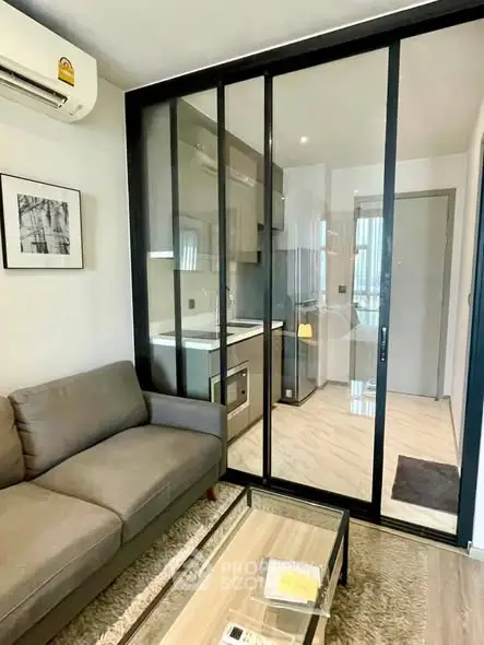 Modern living room with glass partition and compact kitchen in stylish apartment.