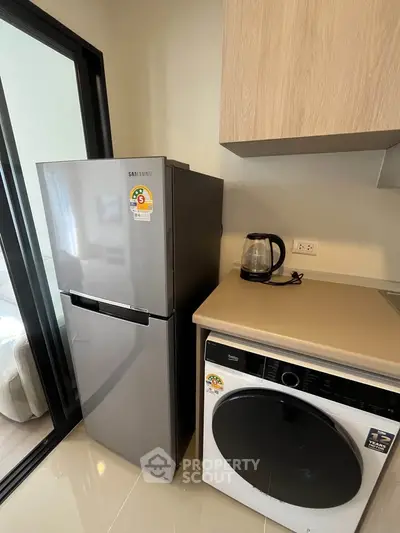 Modern kitchen with sleek fridge and washing machine in compact layout.