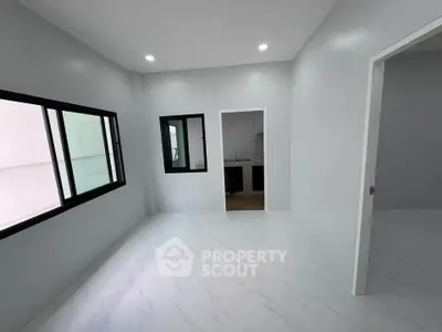 Spacious modern living room with sleek white flooring and large windows, adjacent to a compact kitchen.