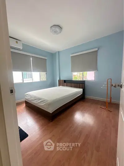 Spacious bedroom with wooden flooring and large windows for natural light