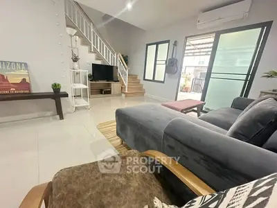 Modern living room with cozy seating and stylish decor, featuring a staircase and large windows for natural light.