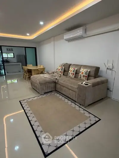 Modern living room with plush sofa and open kitchen layout, featuring sleek design and ambient lighting.