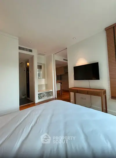 Modern bedroom with wall-mounted TV and wooden accents in a stylish apartment.