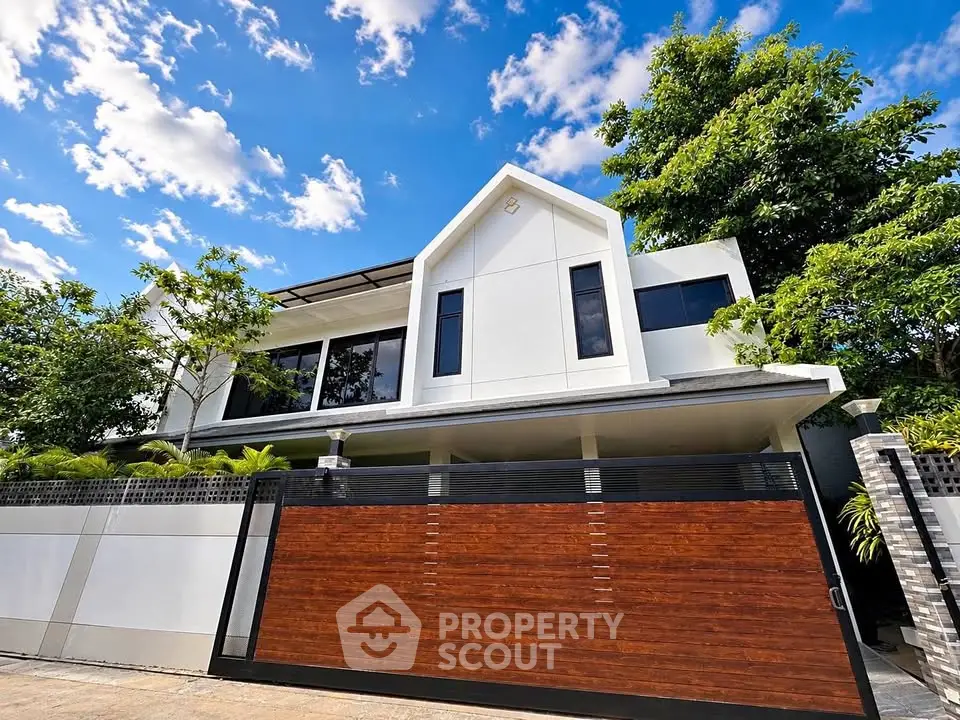 Modern two-story house with sleek design and lush greenery, featuring a stylish wooden gate and clear blue sky.