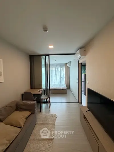 Modern apartment interior with cozy living room and bedroom separated by glass partition.