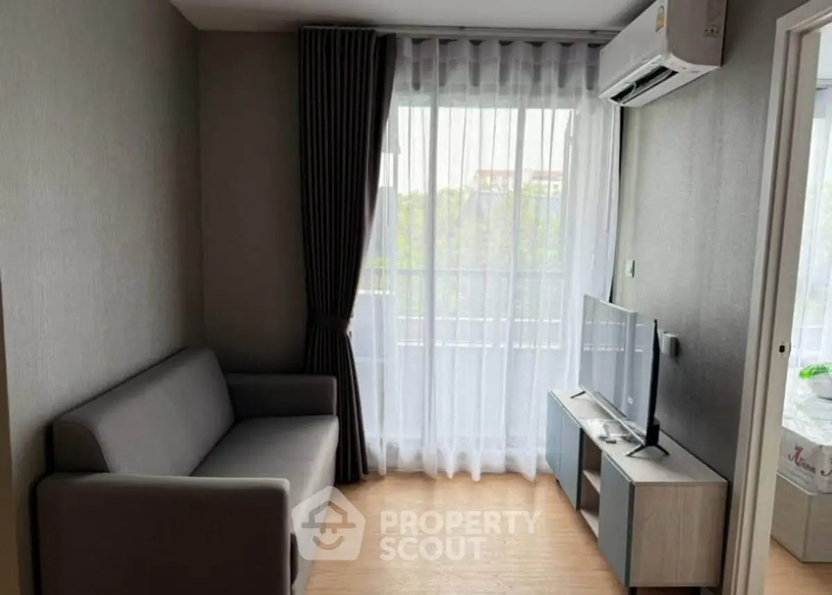 Cozy living room with modern sofa and TV, featuring large window with sheer curtains.