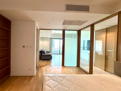 Spacious bedroom with wooden flooring and glass partition leading to a cozy living area.