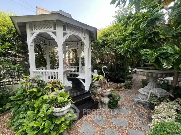 Charming garden gazebo surrounded by lush greenery and stone pathway, perfect for relaxation.