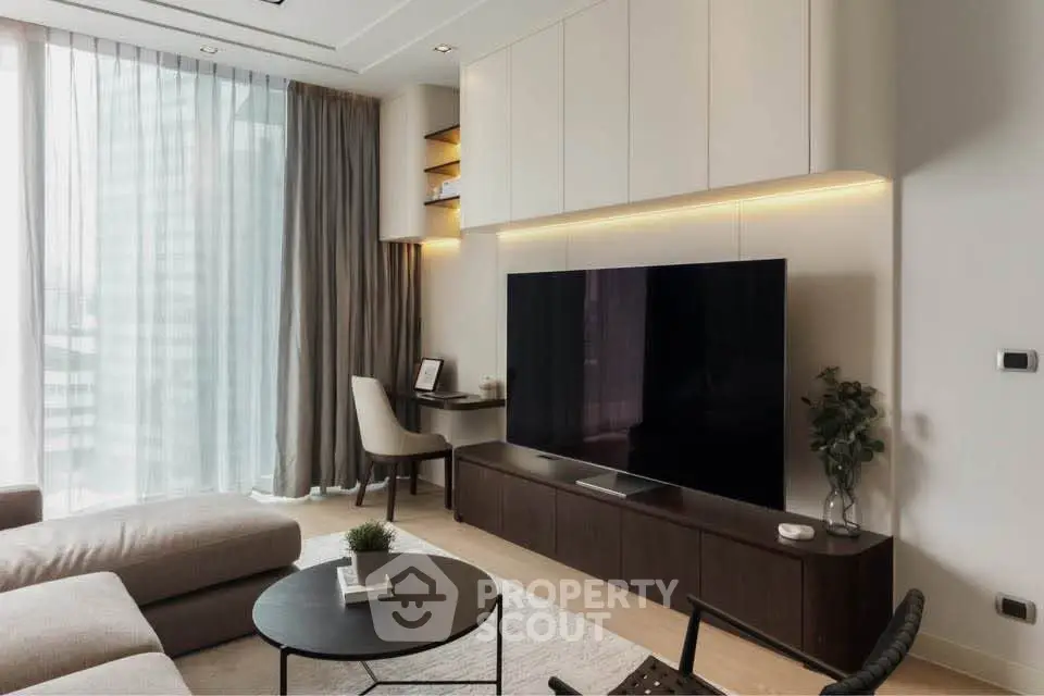Modern living room with large TV, elegant furniture, and floor-to-ceiling windows offering natural light.