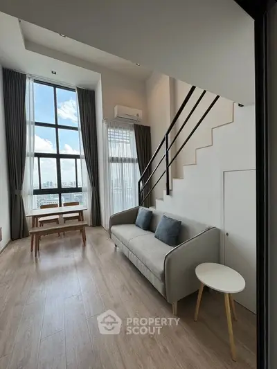Modern loft-style living room with high ceilings and large windows offering city views.
