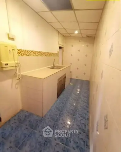 Compact kitchen with blue tiled floor and white walls, featuring a single sink and closed cabinets.