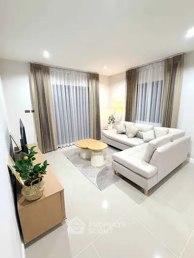 Modern living room with elegant decor, featuring a cozy sectional sofa, stylish coffee table, and large windows with curtains.