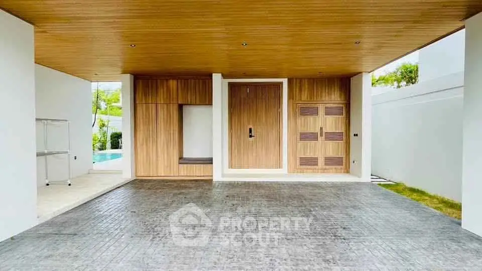 Modern home entrance with wooden accents and pool view, showcasing luxury design.