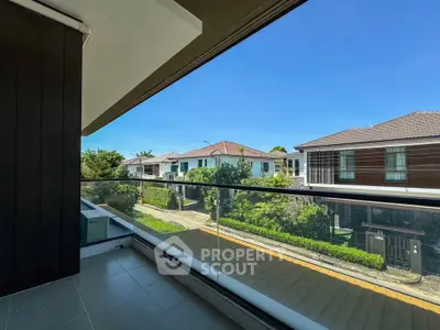 Spacious balcony with glass railing offering a stunning view of modern suburban homes and lush greenery.