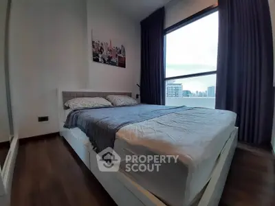 Modern bedroom with large window offering city view, featuring cozy bed and elegant decor.
