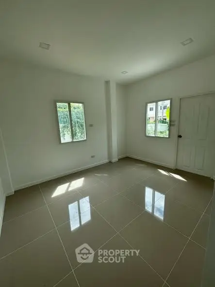 Spacious empty room with tiled flooring and natural light from windows.