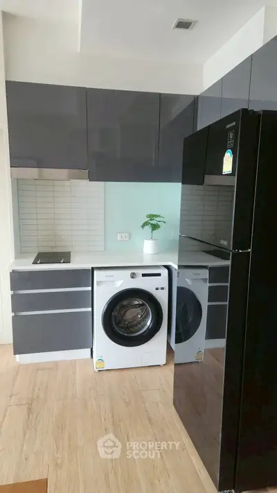 Modern kitchen with sleek cabinets, washing machine, and refrigerator, featuring a minimalist design and light wood flooring.
