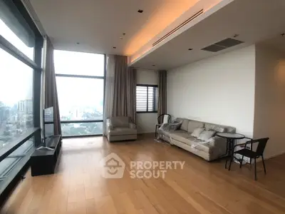Spacious living room with floor-to-ceiling windows offering stunning city views, modern furniture, and wooden flooring.