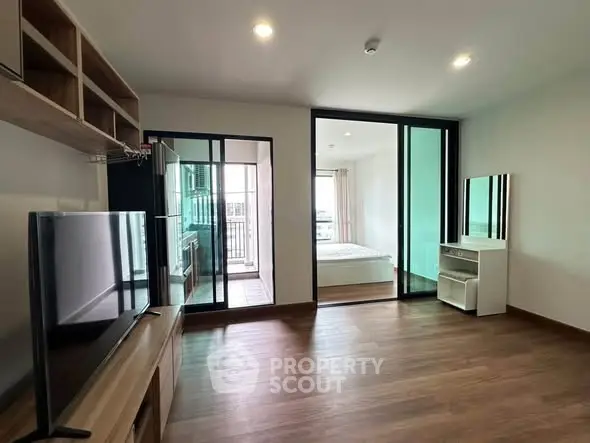 Modern apartment interior with spacious living room and bedroom, featuring sleek wooden flooring and large windows.