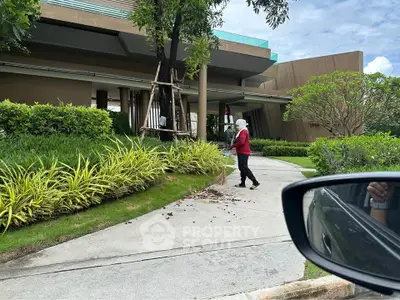 Modern building entrance with lush landscaping and a person maintaining the garden.