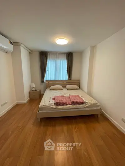 Cozy bedroom with wooden flooring and natural light, featuring a comfortable bed and modern decor.