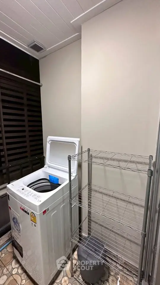 Laundry area with washing machine and metal shelving unit in modern home.