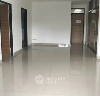 Spacious empty room with glossy tiled flooring and wooden doors, ideal for customization.