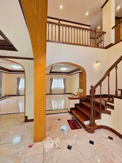 Elegant two-story home with wooden staircase and marble floors, featuring spacious open layout and large windows.