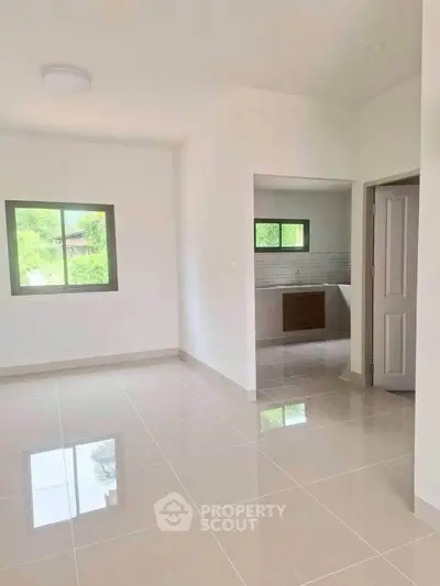 Spacious open-plan living area with tiled floors and natural light, leading to a modern kitchen.