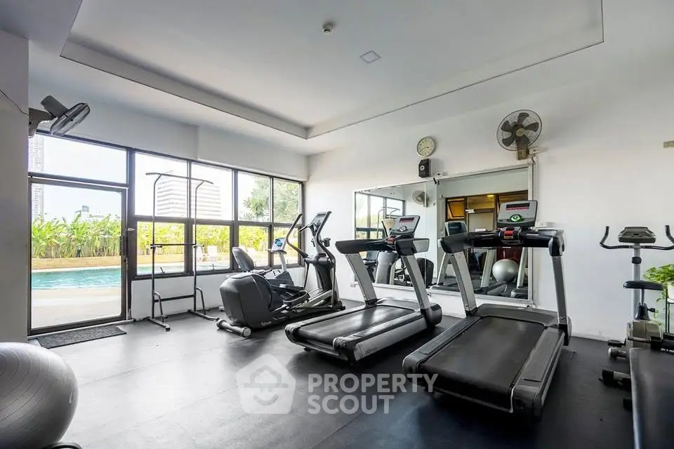 Modern gym with treadmills and exercise equipment overlooking a pool area, ideal for fitness enthusiasts.