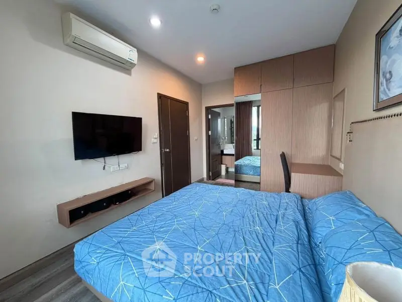 Modern bedroom with blue bedding, wall-mounted TV, and air conditioning unit.