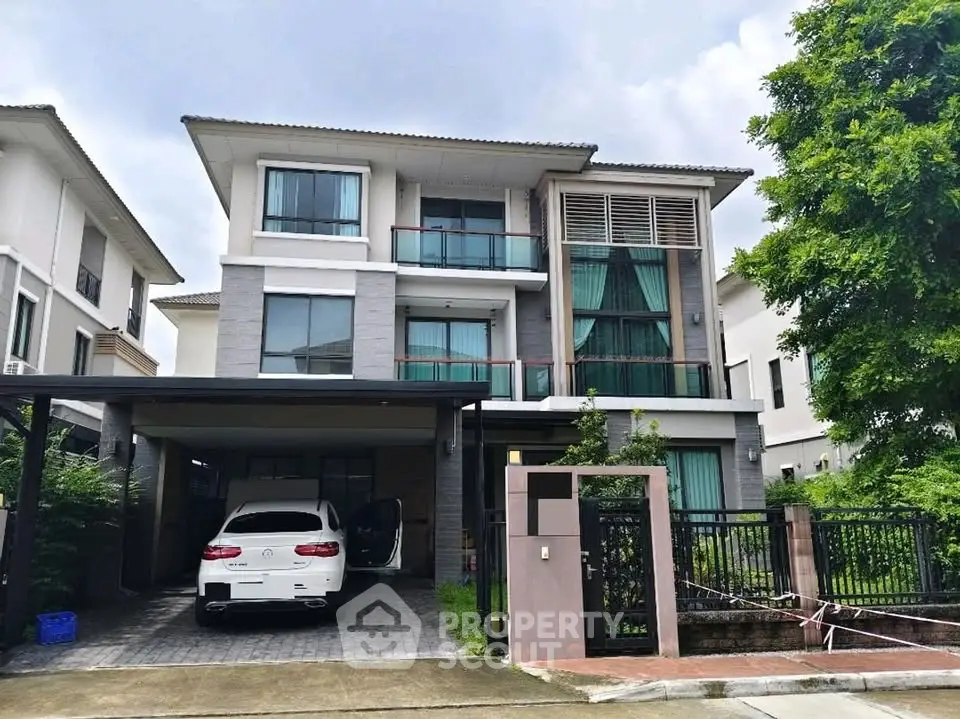 Modern three-story house with carport and lush greenery in a serene neighborhood.