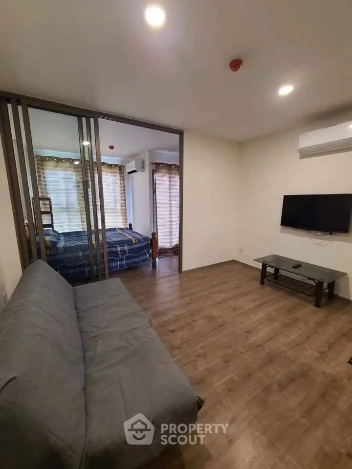 Modern living room with wooden flooring and sliding doors leading to a cozy bedroom.