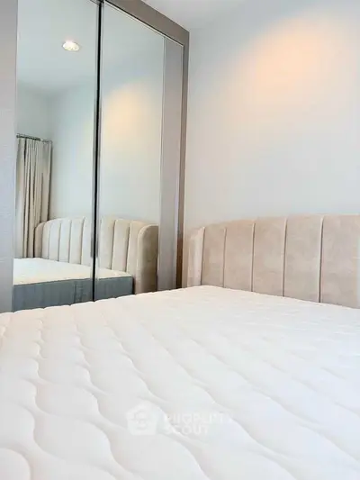 Modern bedroom with plush headboard and mirrored wardrobe in a cozy apartment.