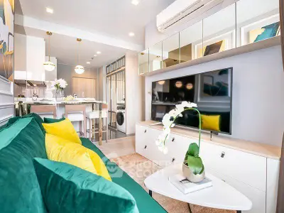 Modern living room with vibrant decor and open kitchen layout, featuring a sleek TV setup and stylish furnishings.
