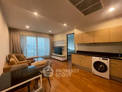 Spacious modern living room with open kitchen and washing machine, featuring wooden flooring and cozy seating area.