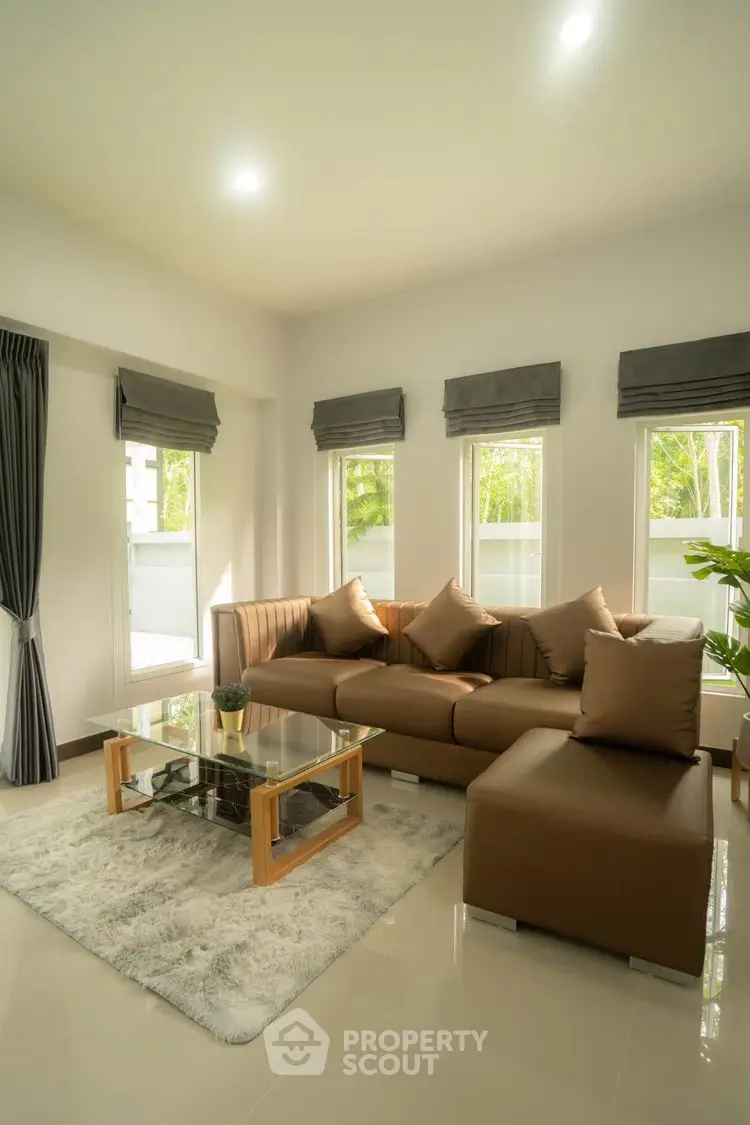 Modern living room with stylish brown sofa and glass coffee table, bright natural light.