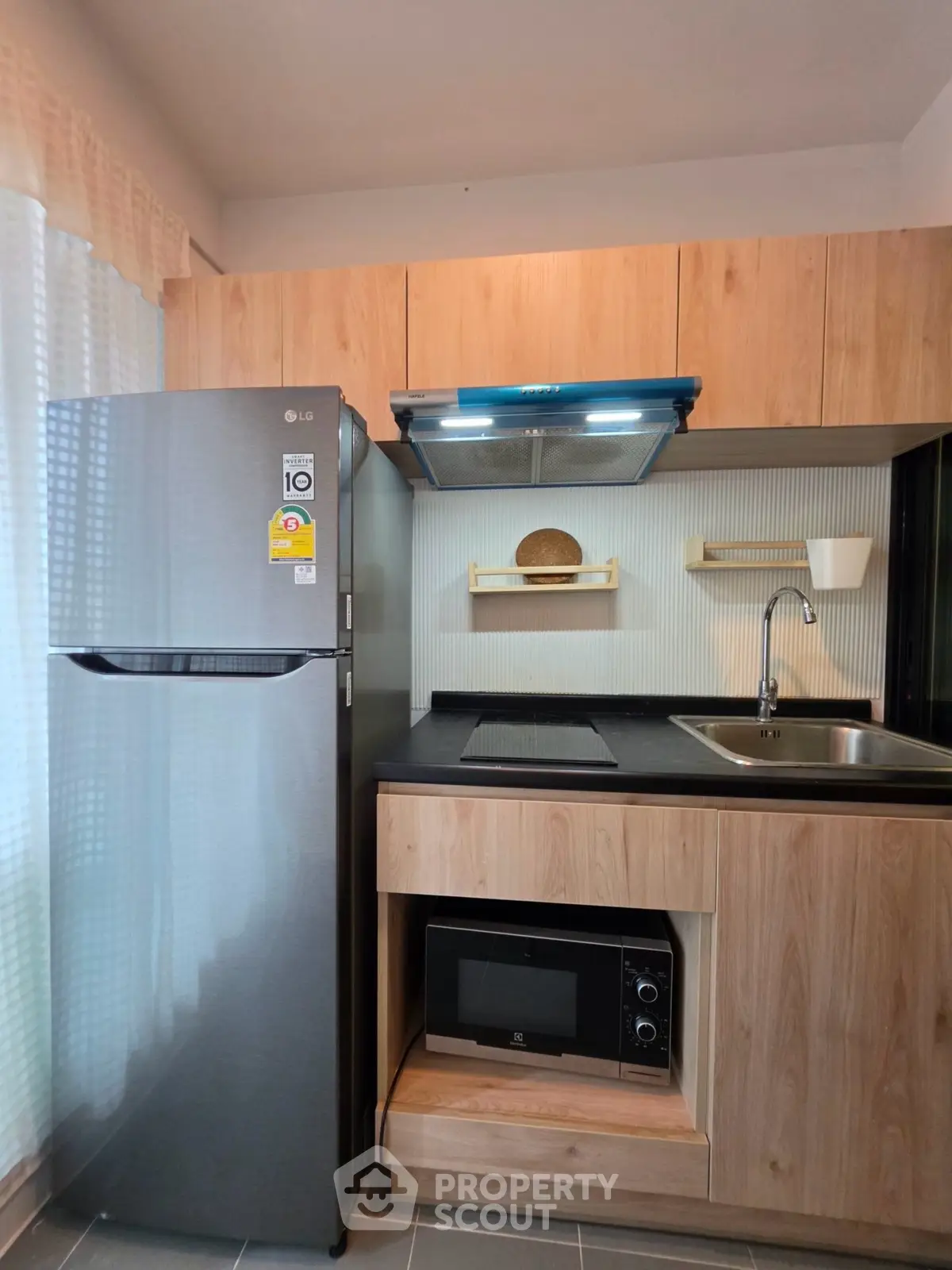 Modern kitchen with sleek appliances and wooden cabinetry, featuring a fridge, microwave, and induction cooktop.