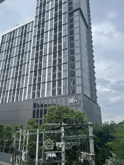 Modern high-rise building with sleek design and lush greenery in urban setting.