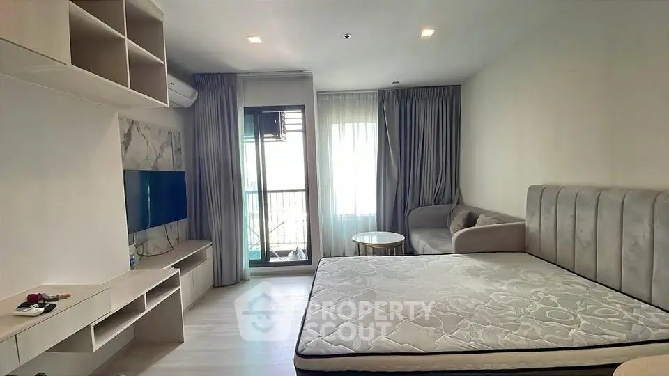 Modern studio apartment with stylish decor and natural light, featuring a cozy bed and sleek entertainment unit.