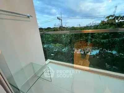 Modern balcony with glass railing offering lush green views and city skyline in the distance.